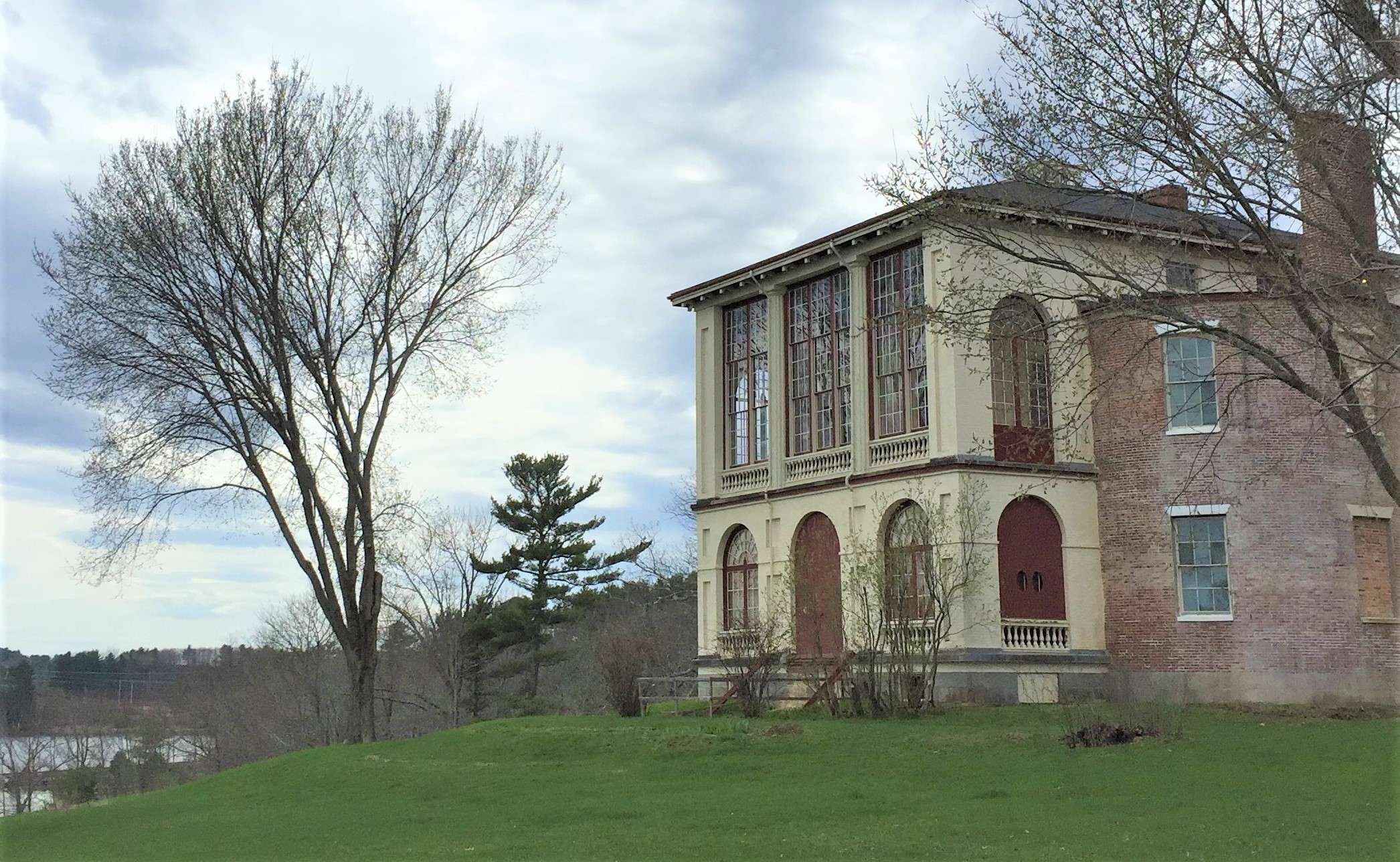 An old house with lots of windows perched on a grassy hill overlooking a bay