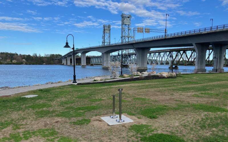 A pretty bare park sits next to a waterway and bridge.