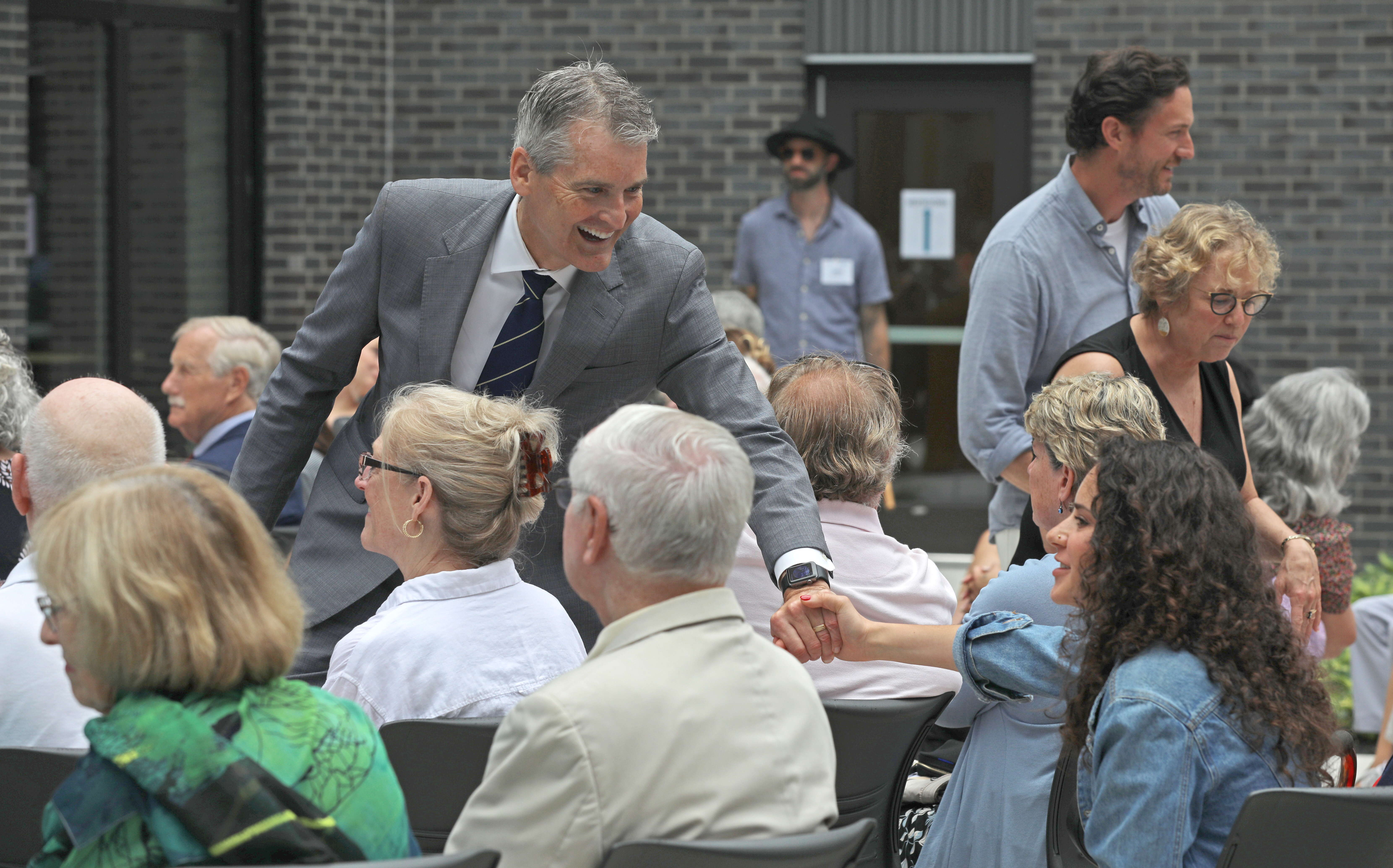 Glenn Cummings shakes hands with a person in a seated crowd.