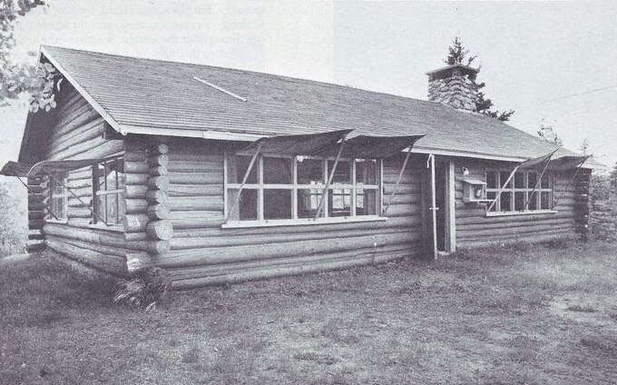 A black-and-white photo shows a log building