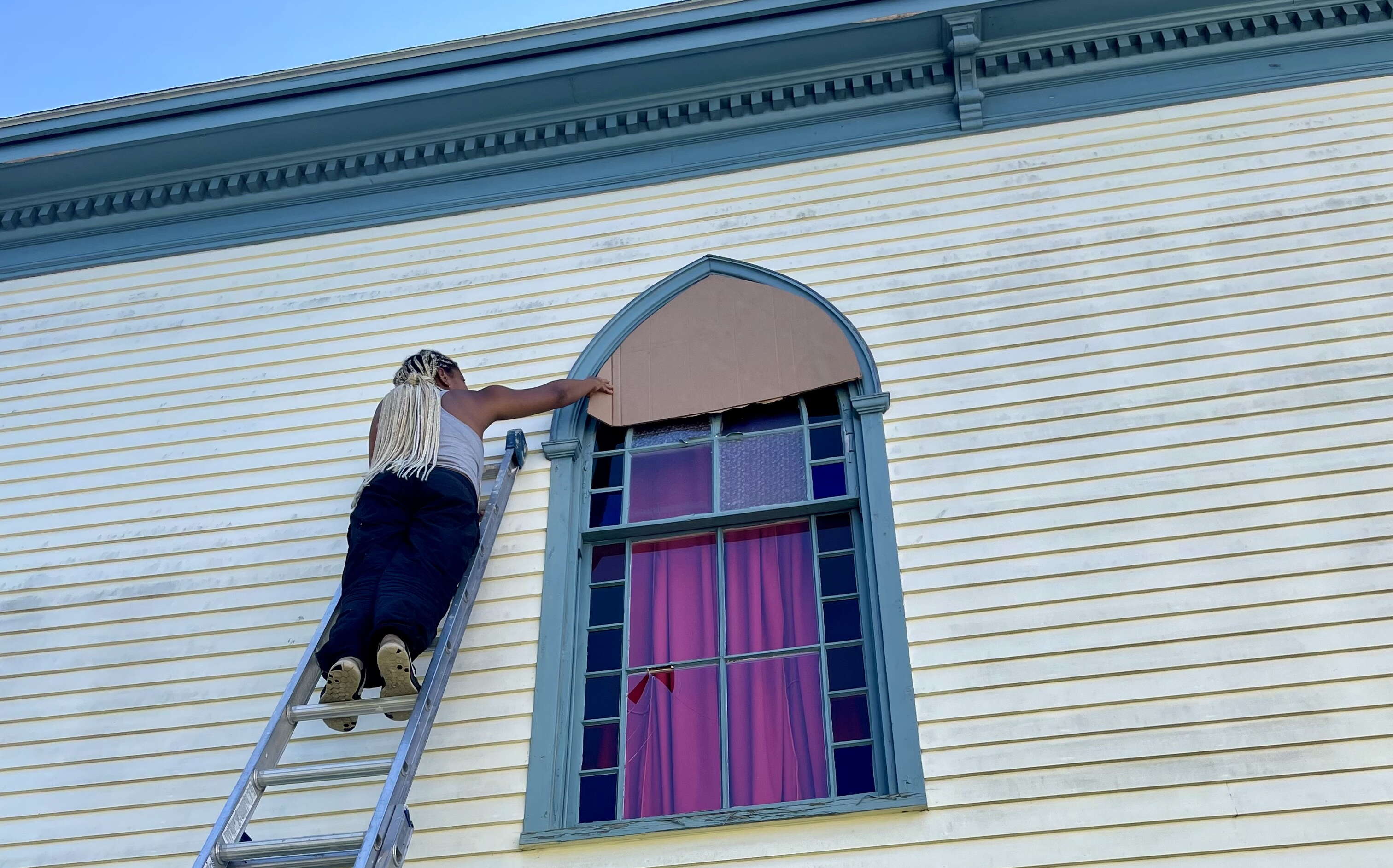 A person is on a ladder outside of Mayo Street Arts.