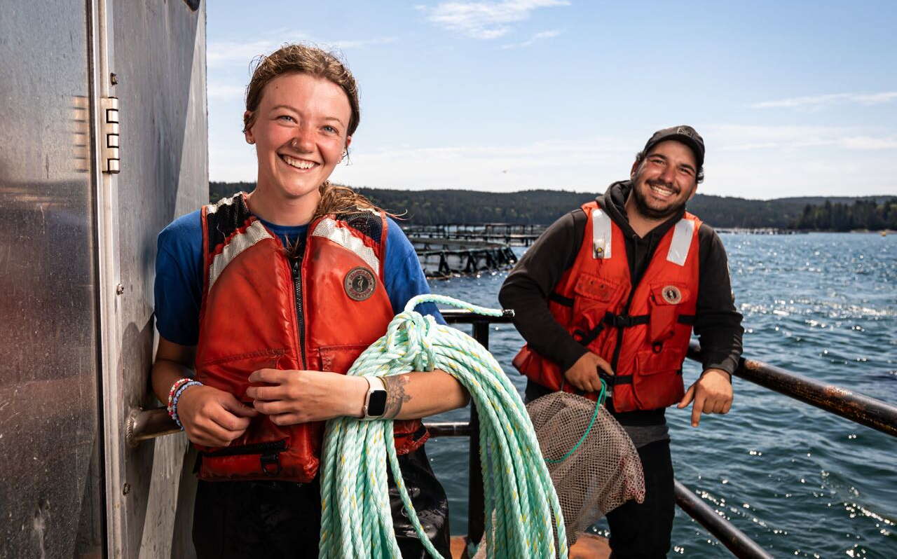 Two people stand on a barge, one holding a coil of rope.