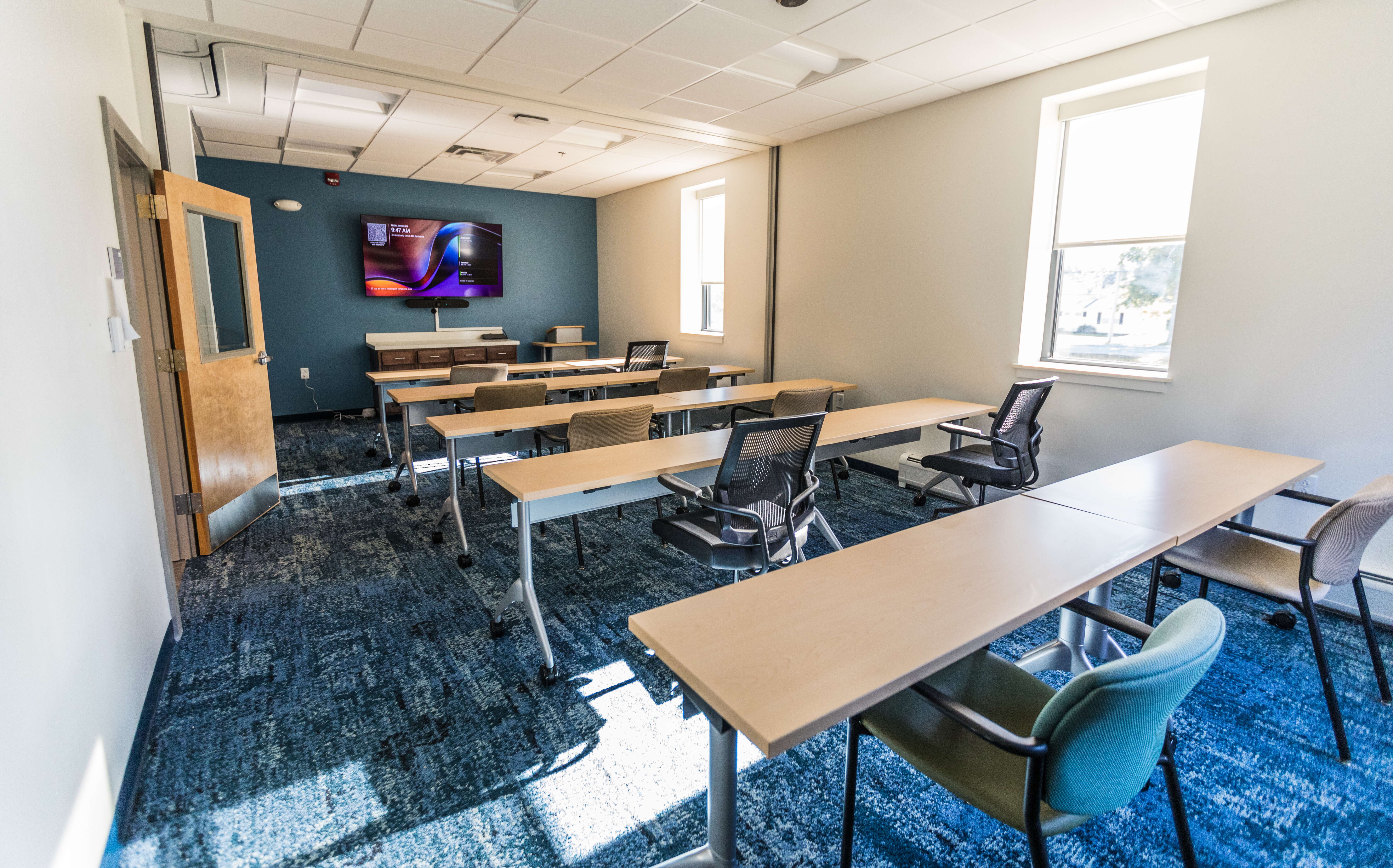 A conference room has long tables, chairs and a TV.