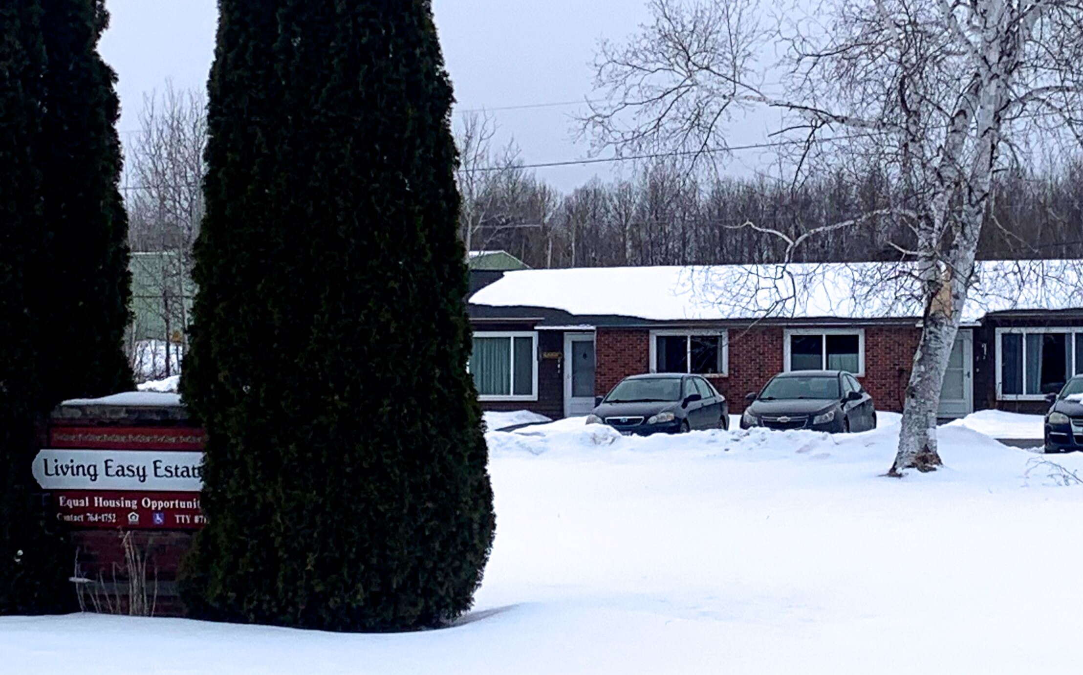 A building in the background and a sign in the foreground around surrounded by snow.