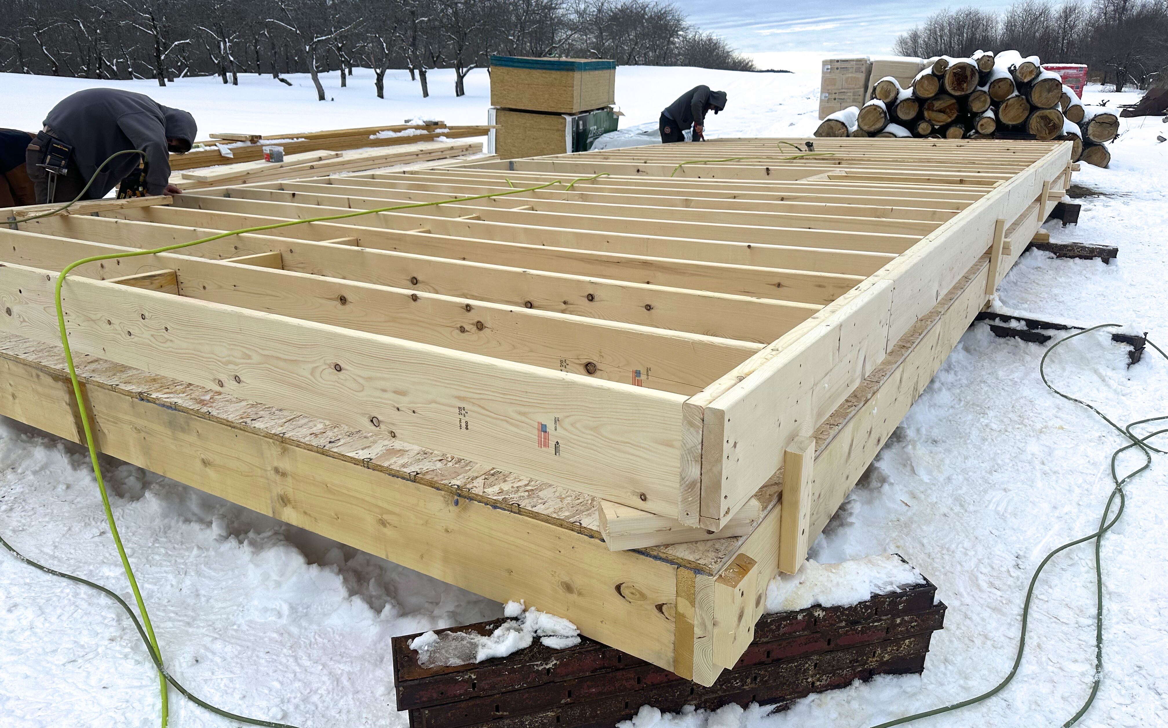 Two people work on a wood structure in the snow.