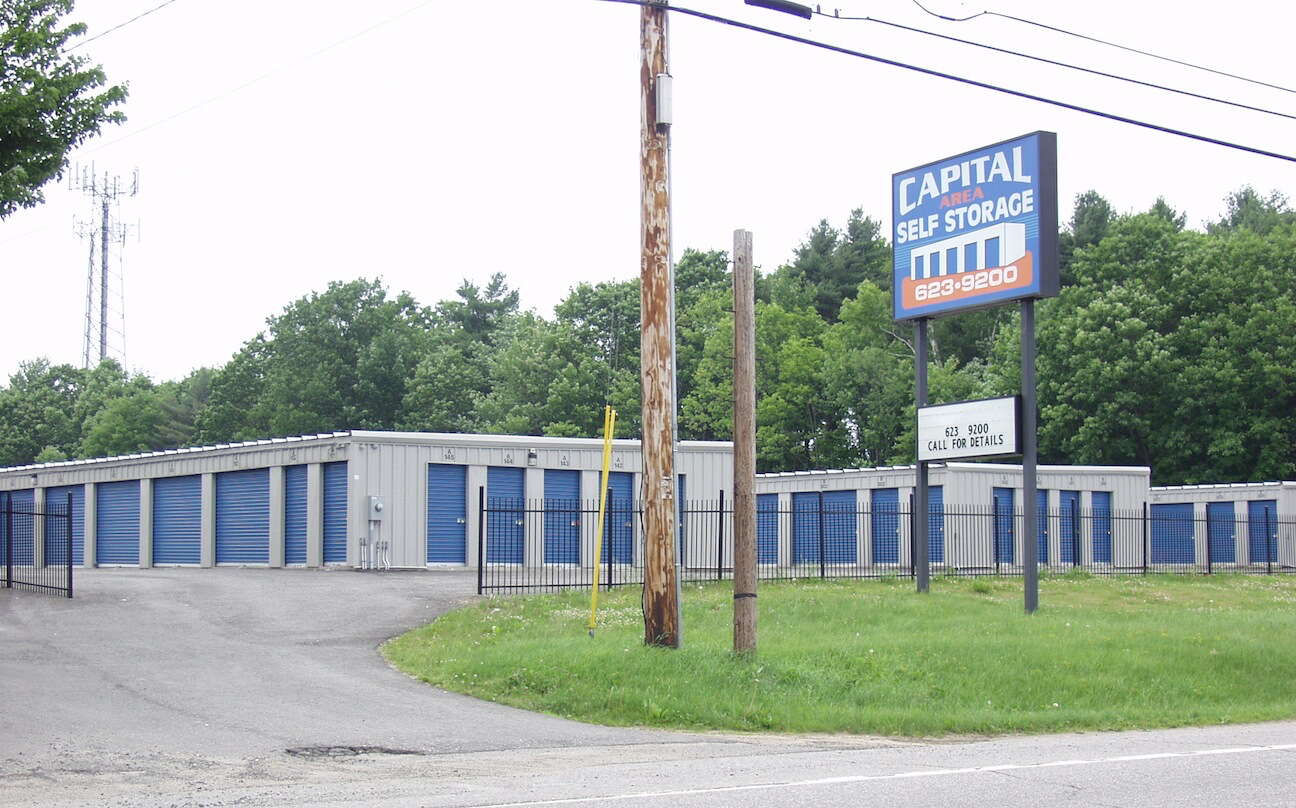 Storage buildings sit behind a fence along a road.