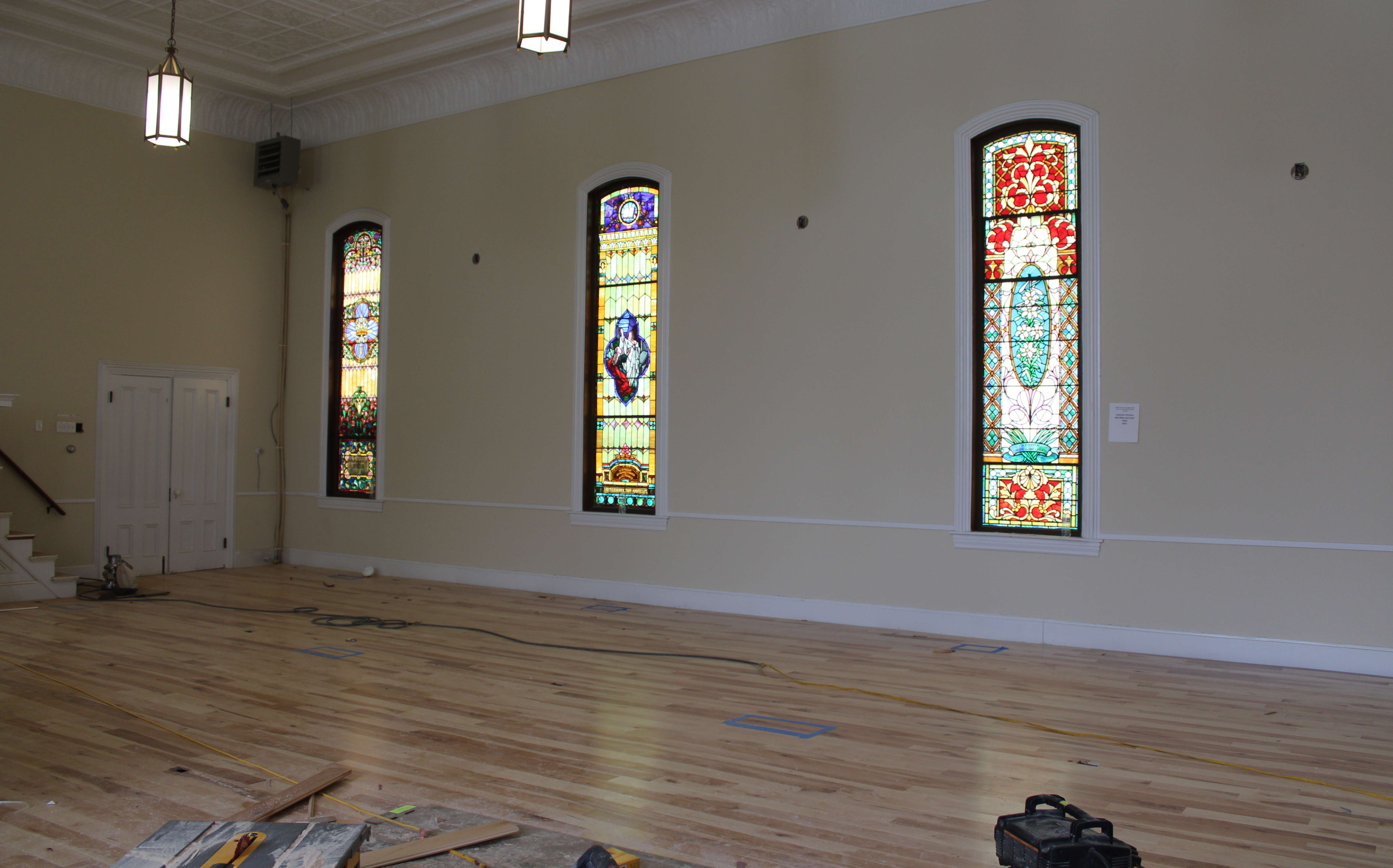 An big interior space has three stained glass windows and a wood floor.