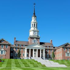 brick building with bell tower and flagpole, students in foreground