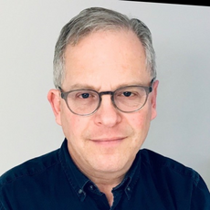 head and shoulders of middle-aged man with gray hair and glasses, in a blue shirt