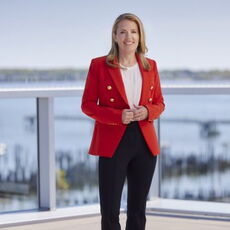 Melissa Smith stands on a deck and wears a red blazer.