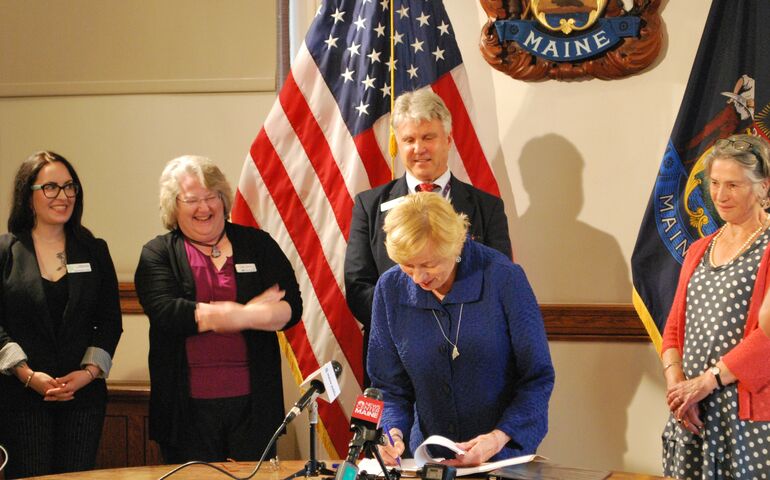 Governor Janet Mill signing a bill surrounded by lawmakers.