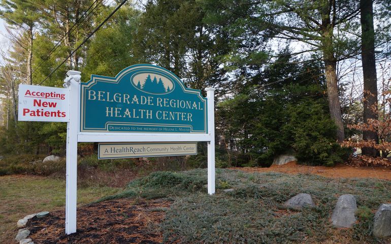 A sign that says Belgrade Regional Health Center, and below that, A Health Read Community Health Center, with a small sign that says accepting new patients, with evergreens behind it