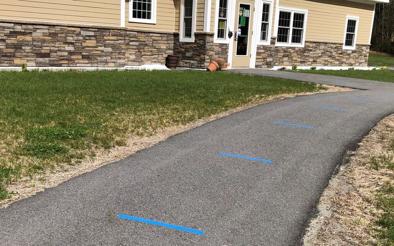 An asphalt sidewalk leading up to a building with blue tape at six-foot intervals