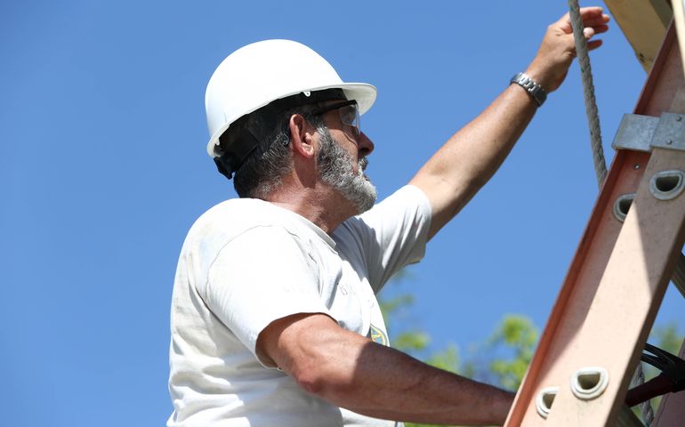 Habitat for Humanity volunteer wearing a hardhat and on a ladder 