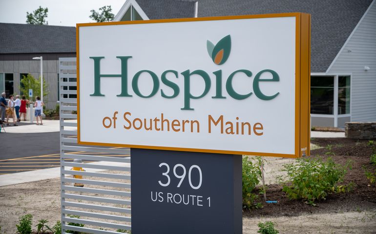 Photo showing Hospice of Southern Maine sign in foreground, people at ribbon cutting in the background 