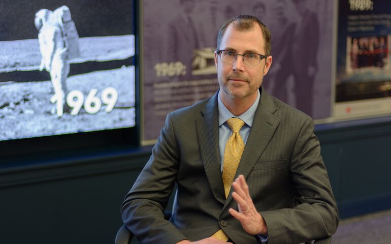 Todd Mason at the Maine Credit Union League headquarters, in front of a screen showing the moon landing.