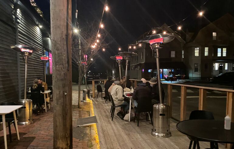 a dark cold looking street with some people bundled in coats eating at outdoor tables