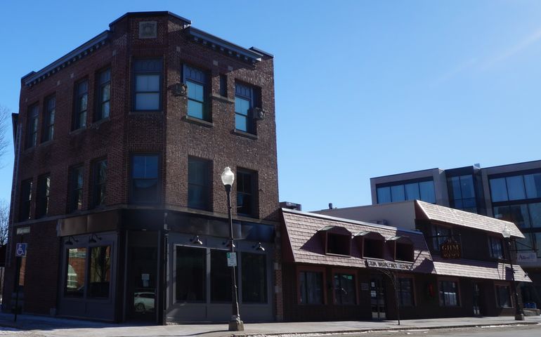 An older brick building on a corner that looks like it had a recent upgrade with a modern four-story building in the background