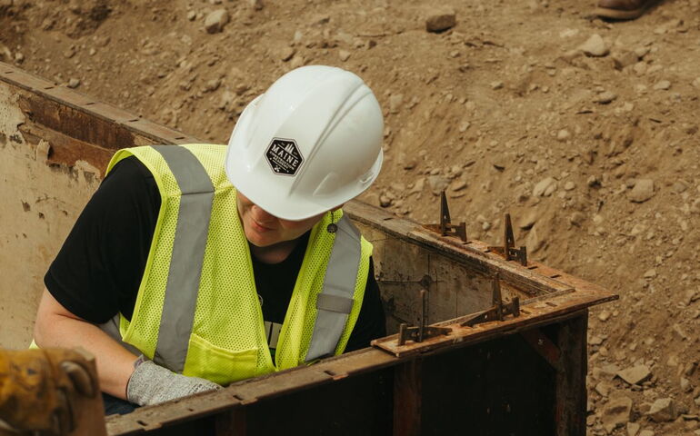 A participant in the Maine Construction Academy is working with steel beams set in a mound of dirt.