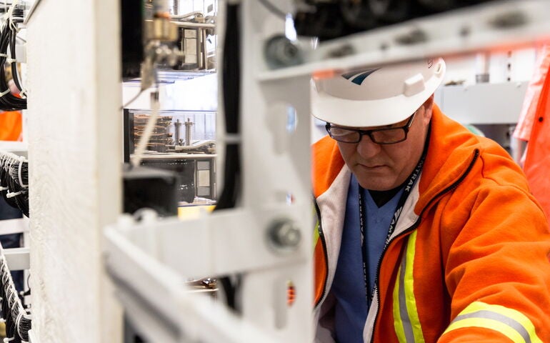 A person in safety gear works on machinery in the Amtrak system.