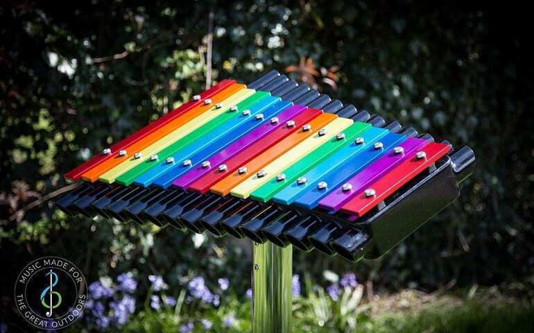 A colorful xylophone is attached to a stand outdoors.