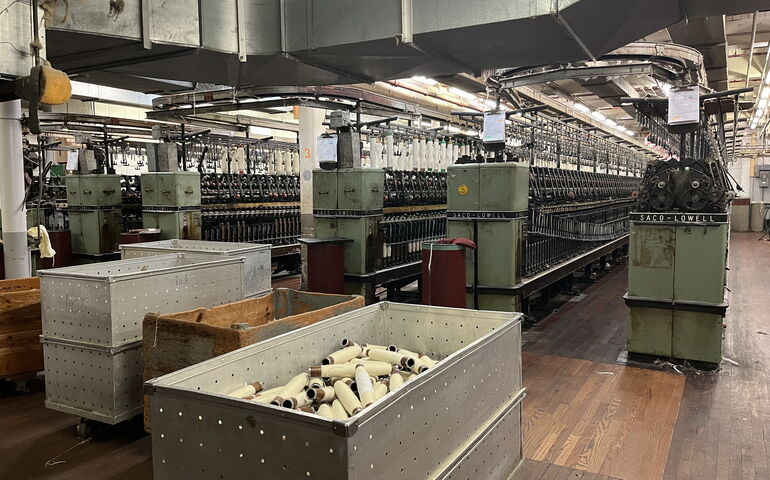The inside of a yarn mill shows lots of machinery and bins.