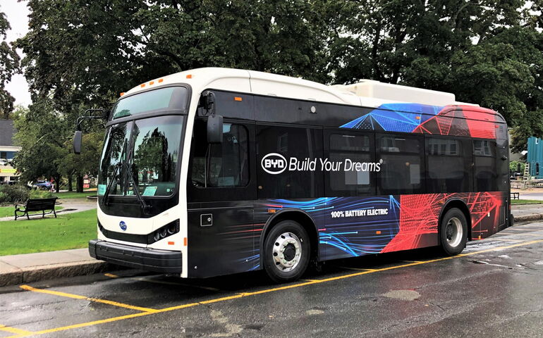 An electric bus is parked near a town green.