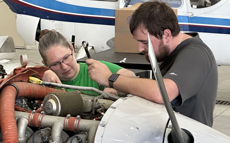 Two people at UMA's aviation school work on a plane.