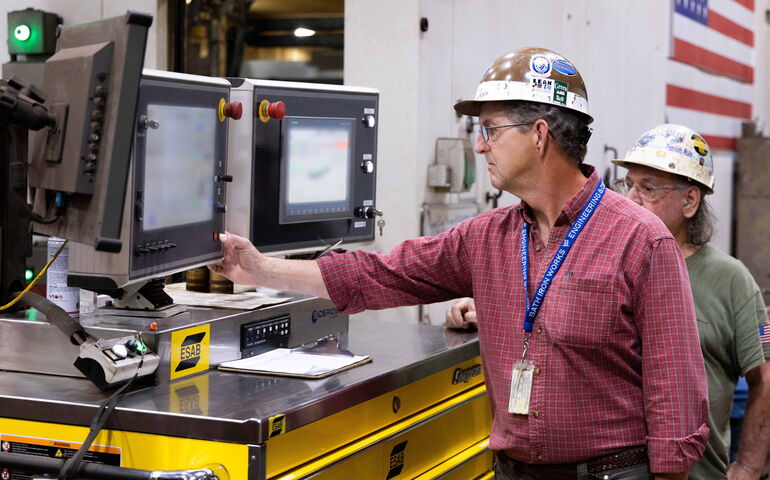 TWo people stand at industrial machinery at BIW.