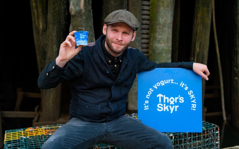Unnar Helgi Danielsson sitting on crates by the water holding up a package of Thor's Skyr 